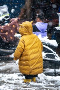 child in yellow jacket with hood standing on snowy sidewalk